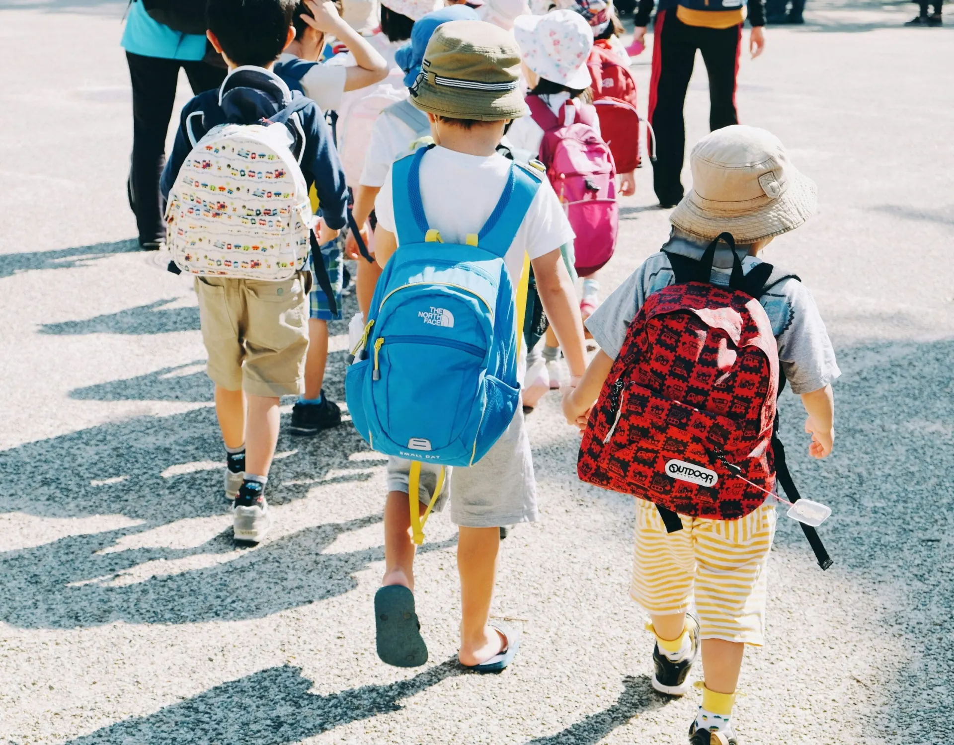 A line of elementary school students wearing backpacks, walking outdoors on a field trip.