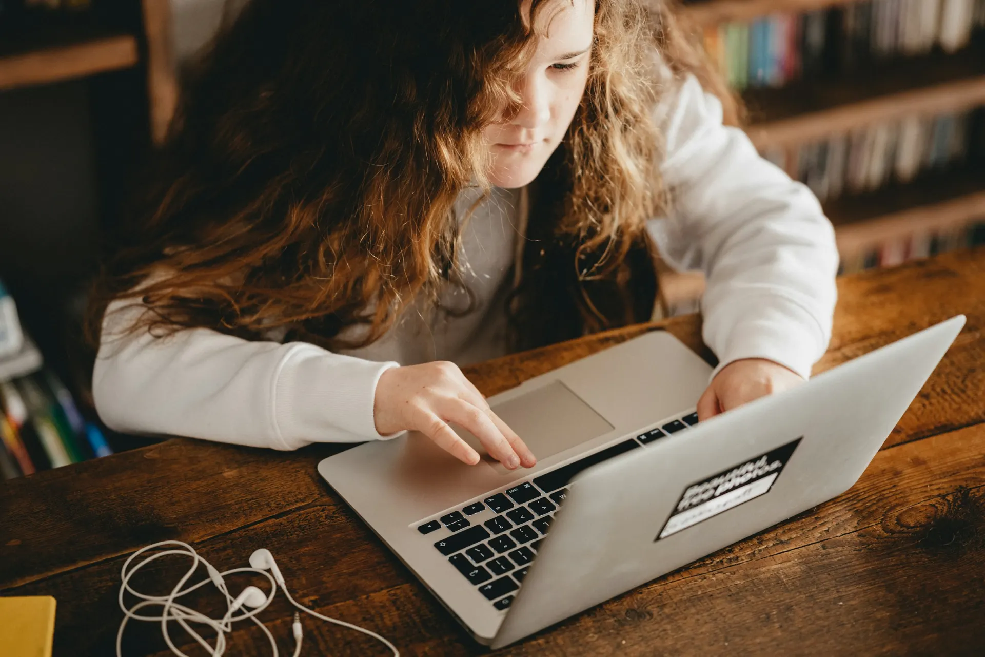 A student writing on a laptop at a wooden table.
